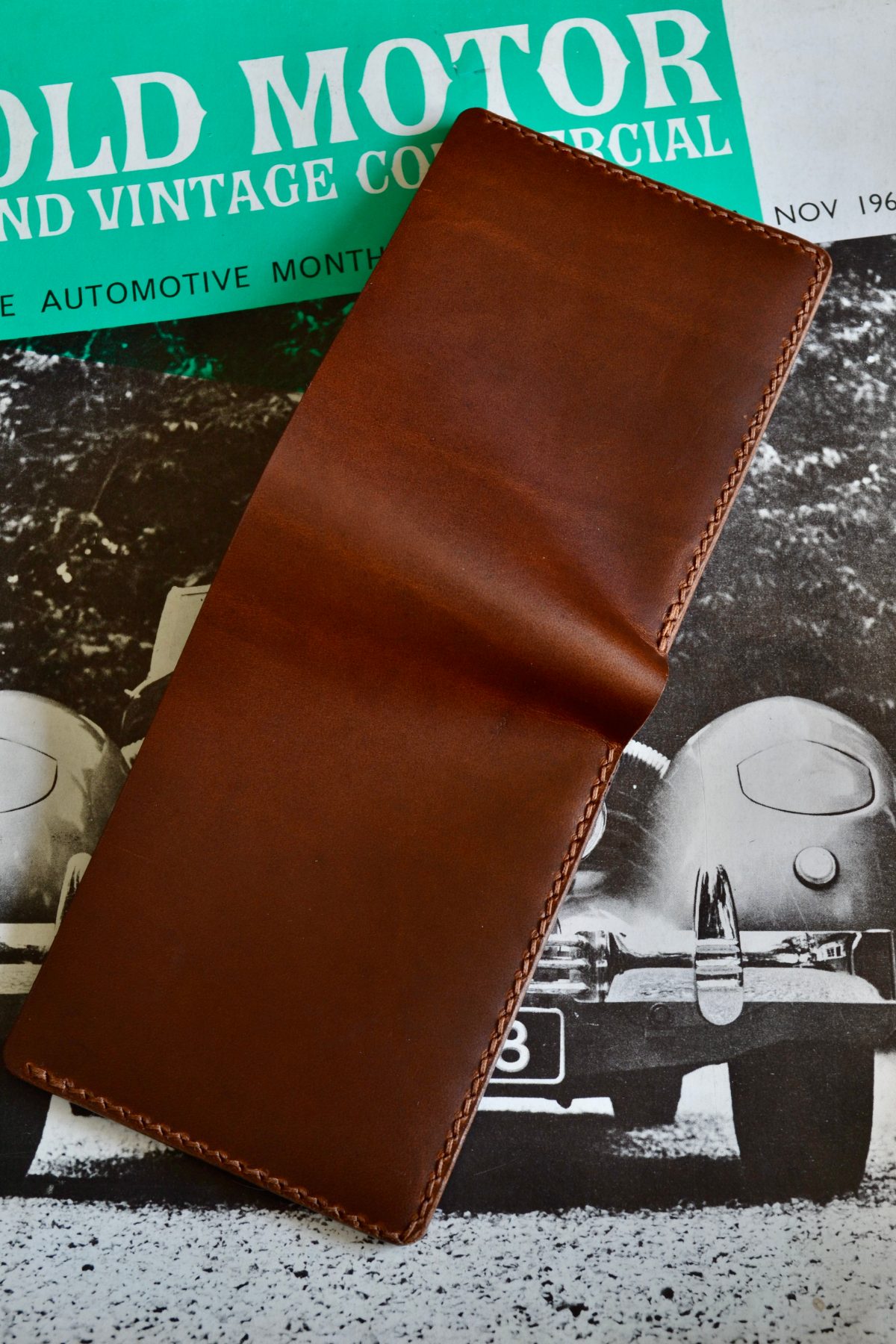 A tan bifold wallet lying open with its outside facing up, stitched right around the edge and creased down the fold