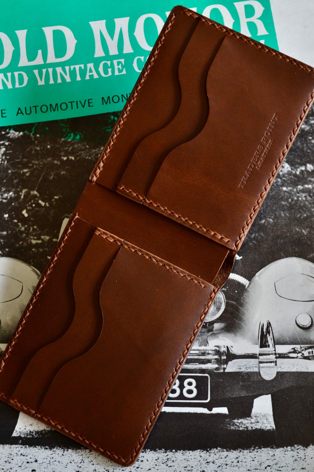 A tan bifold wallet open, two scooped card slots on each panel either side of the fold and the Traders Point Leather mark embossed into the upper panel